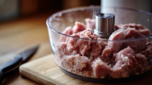 Raw pork and beef being ground in a food processor on a kitchen counter